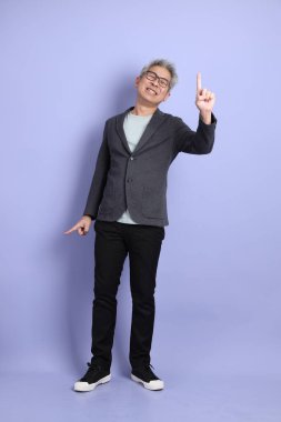 50 'li yılların Asyalı kıdemli iş adamı. Gözlüklü, resmi giyinmiş. Mor arka planda izole edilmiş bir yere işaret ediyor.. 