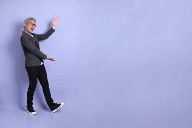 50 'li yılların Asyalı kıdemli iş adamı. Gözlüklü, resmi giyinmiş. Mor arka planda izole edilmiş bir yere işaret ediyor.. 