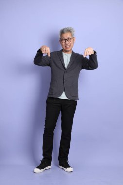 50 'li yılların Asyalı kıdemli iş adamı. Gözlüklü, resmi giyinmiş. Mor arka planda izole edilmiş bir yere işaret ediyor.. 