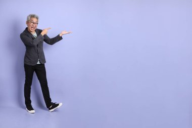 50 'li yılların Asyalı kıdemli iş adamı. Gözlüklü, resmi giyinmiş. Mor arka planda izole edilmiş bir yere işaret ediyor.. 