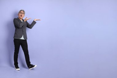 50 'li yılların Asyalı kıdemli iş adamı. Gözlüklü, resmi giyinmiş. Mor arka planda izole edilmiş bir yere işaret ediyor.. 