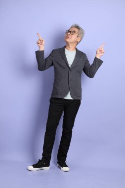 50 'li yılların Asyalı kıdemli iş adamı. Gözlüklü, resmi giyinmiş. Mor arka planda izole edilmiş bir yere işaret ediyor.. 