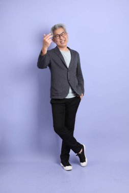 50 'li yılların Asyalı kıdemli iş adamı, gözlüklü, resmi kıyafetli, mor arka planda izole edilmiş bir selamlama jesti.. 