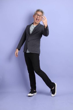 50 'li yılların Asyalı kıdemli iş adamı, gözlüklü, resmi kıyafetli, mor arka planda izole edilmiş bir selamlama jesti.. 