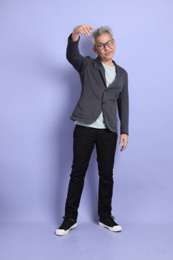 50 'li yılların Asyalı kıdemli iş adamı, gözlüklü, resmi kıyafetli, mor arka planda izole edilmiş bir selamlama jesti.. 