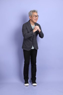 50 'li yılların Asyalı kıdemli iş adamı, gözlüklü, resmi kıyafetli, mor arka planda izole edilmiş bir selamlama jesti.. 