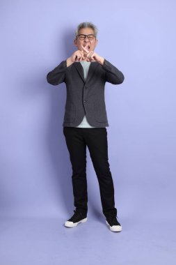 50 'li yılların Asyalı kıdemli iş adamı, gözlüklü, resmi giyinmiş. Durma, yasaklama, mor arka planda izole edilmeyi reddetme jestleriyle.. 