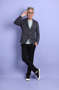 50 'li yılların Asyalı kıdemli iş adamı, gözlüklü, resmi kıyafetli, mor arka planda izole edilmiş bir jestle.. 