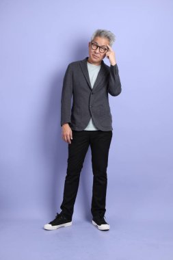 50 'li yılların Asyalı kıdemli iş adamı, gözlüklü, resmi kıyafetli, mor arka planda izole edilmiş bir jestle.. 