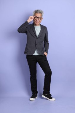 50 'li yılların Asyalı kıdemli iş adamı, gözlüklü, resmi kıyafetli, mor arka planda izole edilmiş bir jestle.. 