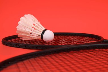 Asyalı adam elinde Badminton raketi ve servis aletini tutuyor ve turuncu arka planda ağa vuruyor. Egzersiz ve spor kavramı.