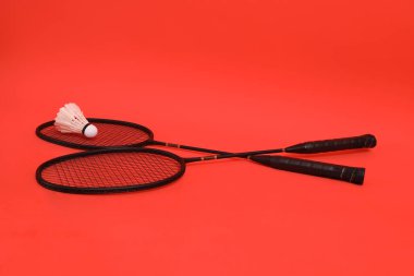 Asyalı adam elinde Badminton raketi ve servis aletini tutuyor ve turuncu arka planda ağa vuruyor. Egzersiz ve spor kavramı.