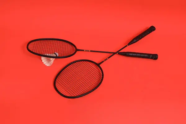 Asyalı adam elinde Badminton raketi ve servis aletini tutuyor ve turuncu arka planda ağa vuruyor. Egzersiz ve spor kavramı.