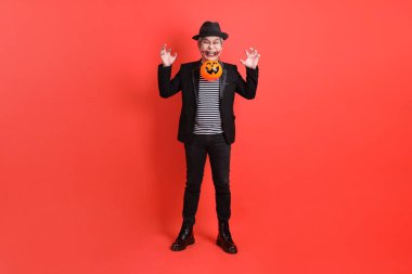 Cadılar Bayramı kostümlü Asyalı son sınıf öğrencisi. El ele tutuşurken turuncu arka planda izole edilmiş balkabağı..