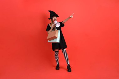 Cadıların Cadılar Bayramı kostümlü genç Asyalı kadın elinde torbayla turuncu arka planda bekletiliyor. Ekim. 