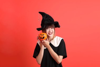 Cadılar Bayramı kostümlü genç Asyalı kadın gülümseyip ayakta dururken turuncu arka planda balkabağı tutuyor. Ekim. 