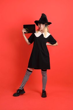 Cadılar Bayramı kostümlü genç Asyalı kadın turuncu arka planda izole edilmiş tablet tutmanın jestini yapıyor. Ekim. 