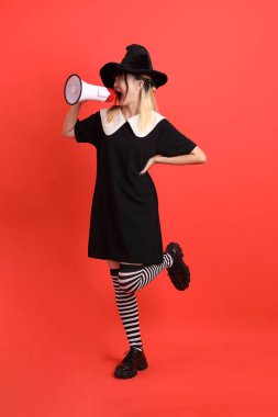 Cadılar Bayramı kostümlü genç Asyalı kadın. Elinde megafonla turuncu arka planda duruyor. Ekim