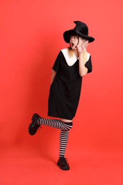 Cadılar Bayramı kostümlü genç Asyalı kadın turuncu arka planda izole edilmiş dinleme ya da işitme hareketi yapıyor. Ekim