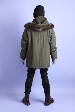 Asyalı son sınıf öğrencisi kışlık kıyafetler giyiyor ve mor arka planda tek başına duruyor..