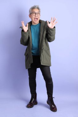 Asyalı son sınıf öğrencisi kışlık kıyafetler giyer. Mor arka planda sürpriz hareketler yapar..