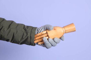 İzole edilmiş mavi arka planda insan eliyle tokalaşan bir manken eli. Sembol, takım çalışması.