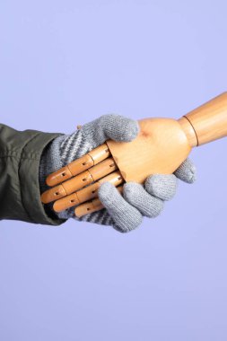 İzole edilmiş mavi arka planda insan eliyle tokalaşan bir manken eli. Sembol, takım çalışması.