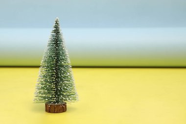 Sarı ve mavi arka planda izole edilmiş küçük dekoratif bir Noel ağacı.