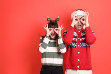 Genç bir Asyalı kadın ve kışın giydiği giysiler, kırmızı arka planda izole edilmiş, gülümseyerek ya da gülümseyerek onaylanmış. Xmas, Noel Baba, Mutlu yıllar.