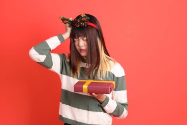 Noel Baba şapkası takmış Asyalı bir kadın elinde bir yığın hediyeyle kırmızı arka planda izole edilmiş bir düşünce jesti yapıyor. Noel Baba! Noel Baba!.