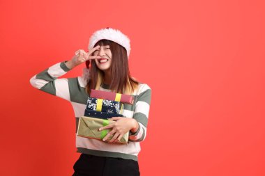 Noel Baba şapkası takan Asyalı bir kadın elinde iki parmak ya da kırmızı arka planda izole edilmiş Ziyaretçi işareti olan hediyeler tutuyor. Noel Baba! Noel Baba!.