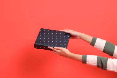 Yeşil çizgili süveter giyen bir el, kırmızı arka planda izole edilmiş bir hediye ya da hediye kutusu tutuyor. Mutlu Noeller..