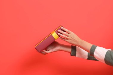 Yeşil çizgili süveter giyen bir el, kırmızı arka planda izole edilmiş bir hediye ya da hediye kutusu tutuyor. Mutlu Noeller..