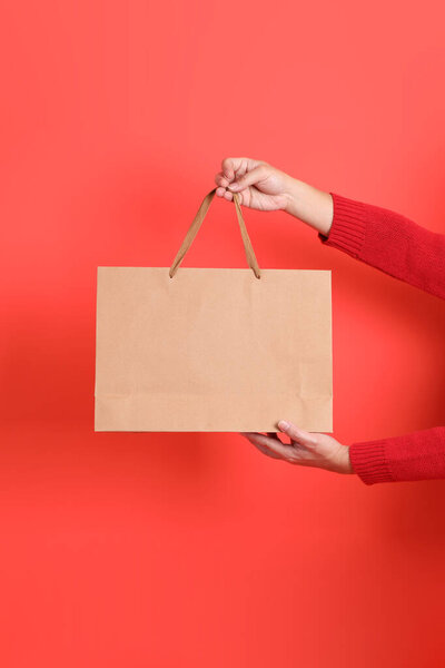 Крупный план руки в красном кардигане, держащем сумку с покупками, на красном фоне. Счастливого Рождества!.