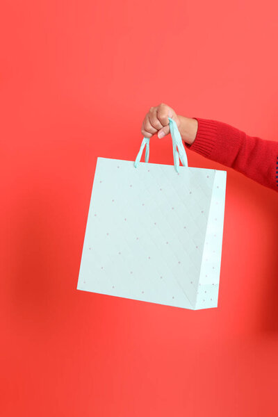 Крупный план руки в красном кардигане, держащем сумку с покупками, на красном фоне. Счастливого Рождества!.