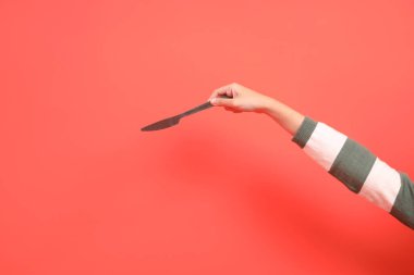 Kırmızı arka planda izole edilmiş, yeşil çizgili kazak giyen, elinde bıçak ya da hediye kutusu olan bir elin yakın çekimi. Mutlu Noeller..