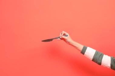 Kırmızı arka planda izole edilmiş, yeşil çizgili kazak giyen, elinde bıçak ya da hediye kutusu olan bir elin yakın çekimi. Mutlu Noeller..