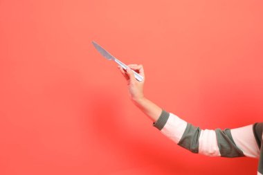 Kırmızı arka planda izole edilmiş, yeşil çizgili kazak giyen, elinde bıçak ya da hediye kutusu olan bir elin yakın çekimi. Mutlu Noeller..