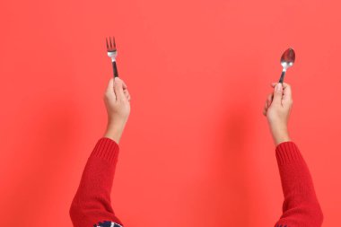 Kırmızı bir hırka giyen, elinde çatal ya da kaşıkla kırmızı bir arka planda izole edilmiş bir el. Mutlu Noeller..