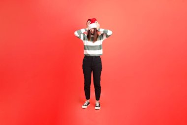 Kırmızı arka planda, Noel Baba şapkalı ve baş ağrısı jestli Asyalı kadın. Noel Baba! Noel Baba!.