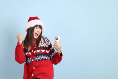 Kırmızı arka planda Noel Baba şapkalı ve cep telefonu tutan Asyalı bir kadın. Noel Baba.