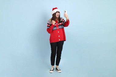 Kırmızı arka planda Noel Baba şapkalı ve cep telefonu tutan Asyalı bir kadın. Noel Baba.