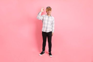 2025 numaralı sıradan görünümlü Asyalı son sınıf öğrencisi. Yeni yıl gözlüklü, süslü gözlüklü, baş parmak hareketli, tamam ya da pembe arka planda izole edilmiş..