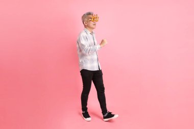 2025 numaralı sıradan görünüşlü Asyalı son sınıf öğrencisi. Yeni yıl gözlüklü, 2025 numara. Pembe arka planda izole edilmiş yürüyüş jesti..