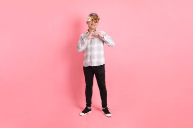 2025 numaralı sıradan görünümlü Asyalı son sınıf öğrencisi. Yeni yıl gözlüğü, kalp şeklinde jestler, küçük kalp, pembe arka planda izole edilmiş aşk..