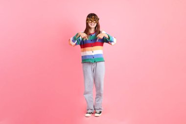 2025 numaralı renkli kış kıyafetleri giyen Asyalı kadın. Yeni yıl gözlüğü. Pembe arka planda izole edilmiş bir işaret..