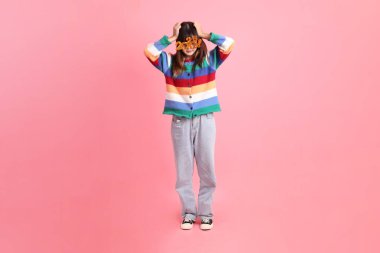 2025 numaralı renkli kış kıyafetleri giyen Asyalı kadın. Yeni yıl gözlüğü. Pembe arka planda izole edilmiş stres hareketi..