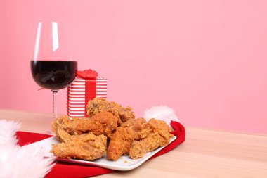 Küçük dekore edilmiş Noel ağacı, bir tabak kızarmış tavuk ve ahşap masada bir bardak kırmızı şarap olan Japon Noel Masası. Bir el pembe arka planda izole edilmiş bir tavuk parçası alıyor. Şükran Günü