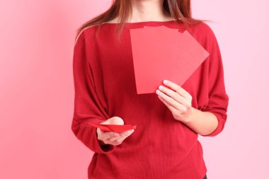 Mutlu Çin Yeni Yılları, pembe arka planda Çin kırmızı zarfları tutan kırmızı tişörtlü Asyalı bir kadının eli.. 