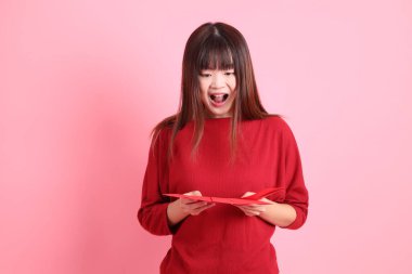 Mutlu Çin Yeni Yılı, pembe arka planda Çin kırmızısı zarflar tutan kırmızı tişörtlü Asyalı bir kadın. Gen Z